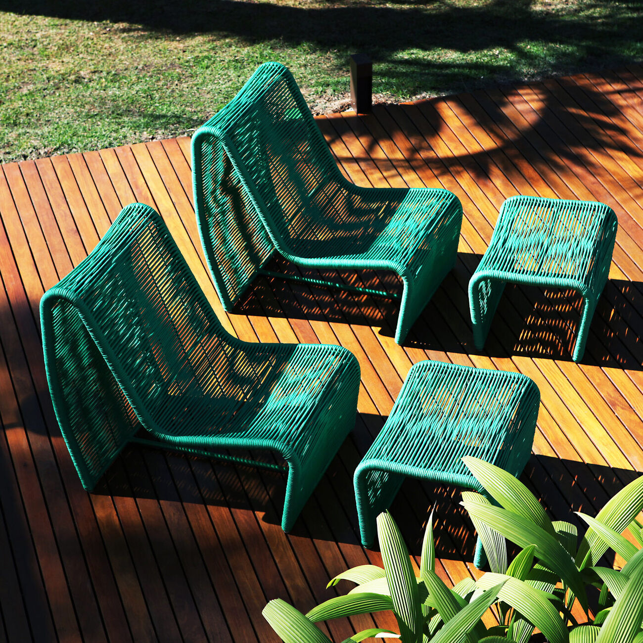 Duas poltronas Pão de Açúcar e dois puffs em corda náutica verde, sobre um deck de madeira ao ar livre, ao lado de uma piscina